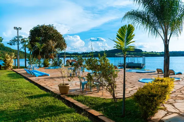 Jardim e deck de pedra com palmeiras e piscinas à beira do Lago de Furnas na Pousada Solar Dona Dora