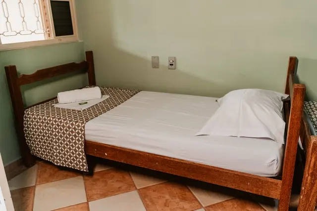 Cama de solteiro de madeira junto à janela em suíte aconchegante da pousada